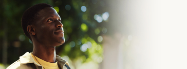 Young man looking up and smiling outdoors under sunlit trees